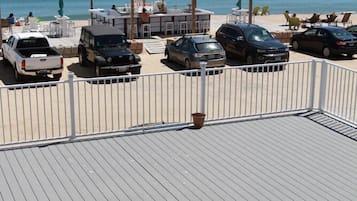 Terraza frente a la playa con vista al océano, varios vehículos estacionados y zonas de estar al aire libre.