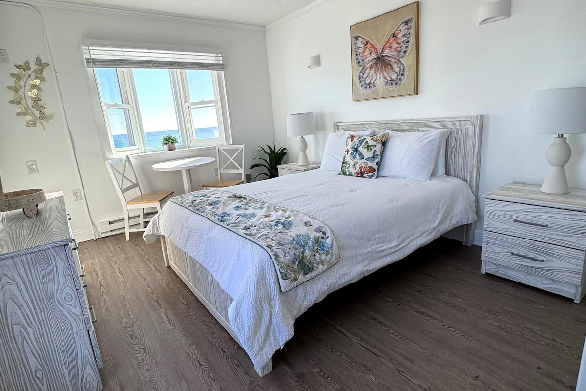A bedroom with a large bed, bedside tables, a desk, and a window with a view.