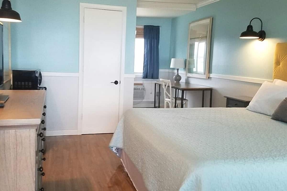 A bedroom with a bed, a desk, a chair, and a lamp.