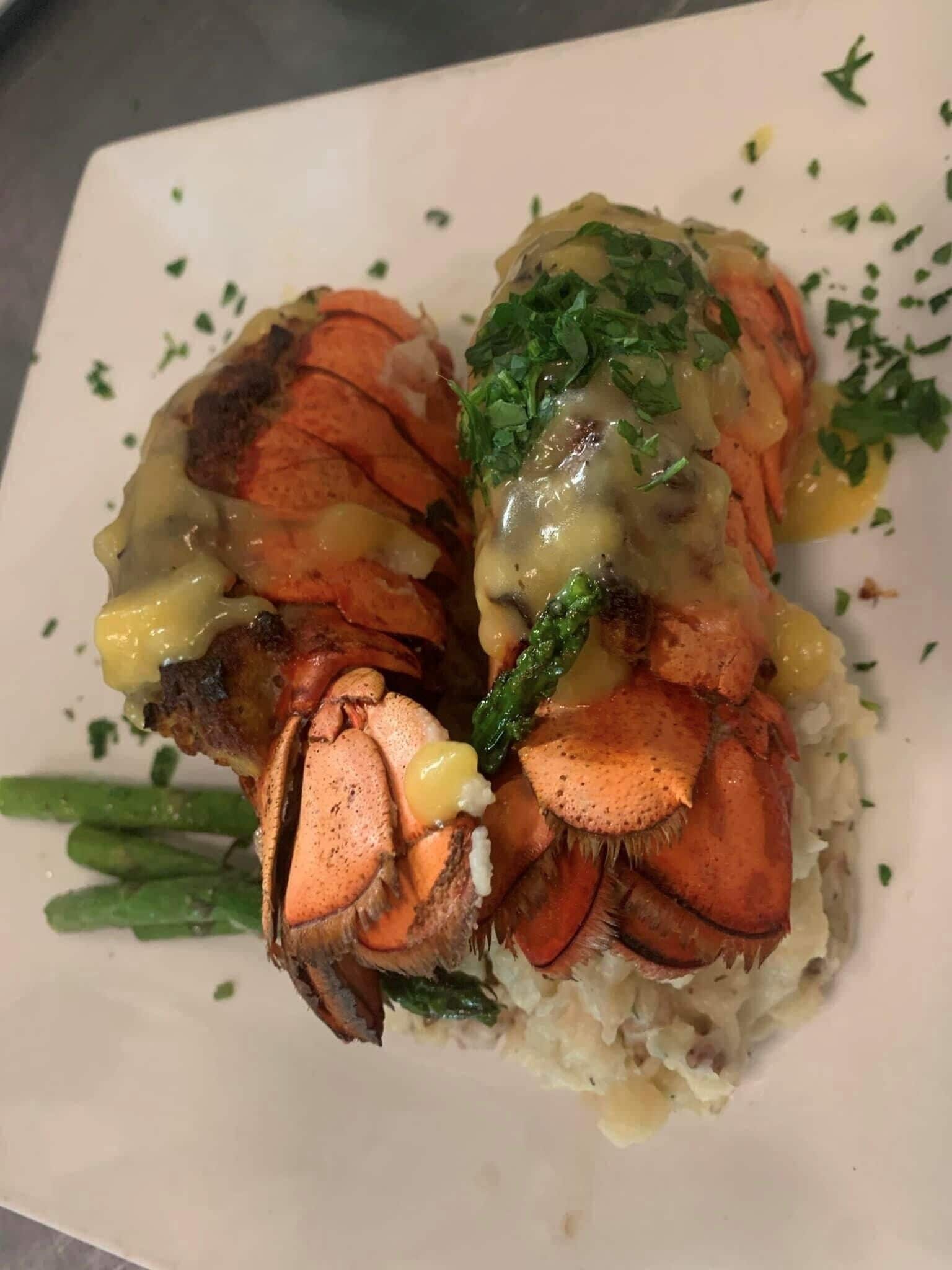 A plate with a lobster tail, green beans, and a creamy sauce.