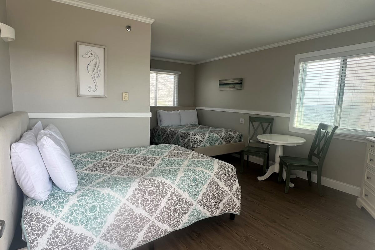 A compact room with two beds, a small table, and a chair.