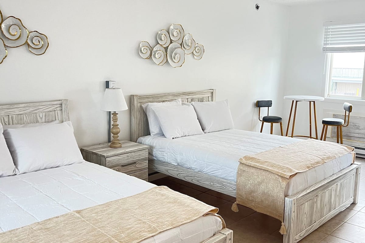 A bedroom with two beds, a nightstand, a lamp, and a decorative wall piece.