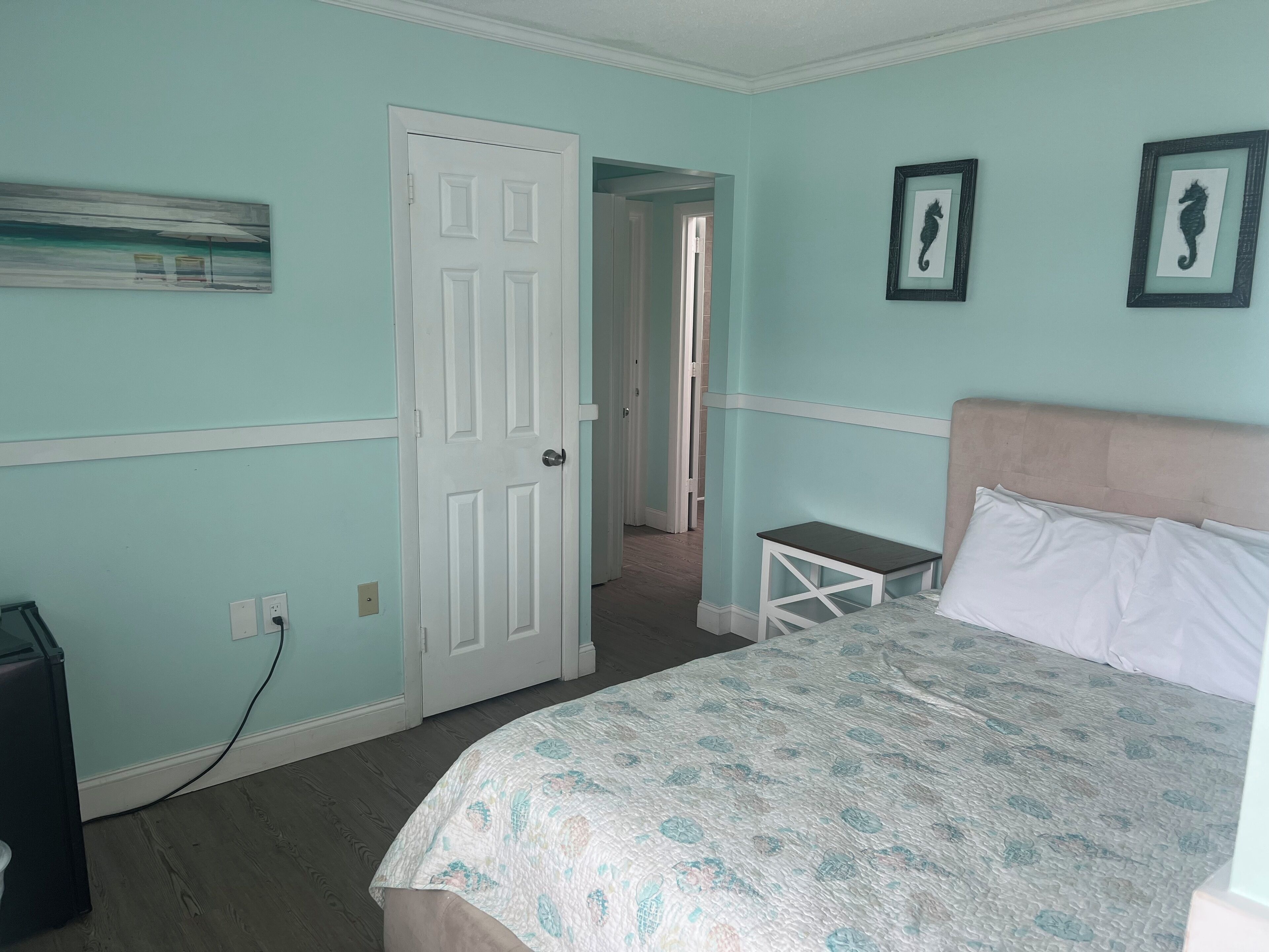 A bedroom with a bed, a door, a small table, and two framed pictures on the wall.
