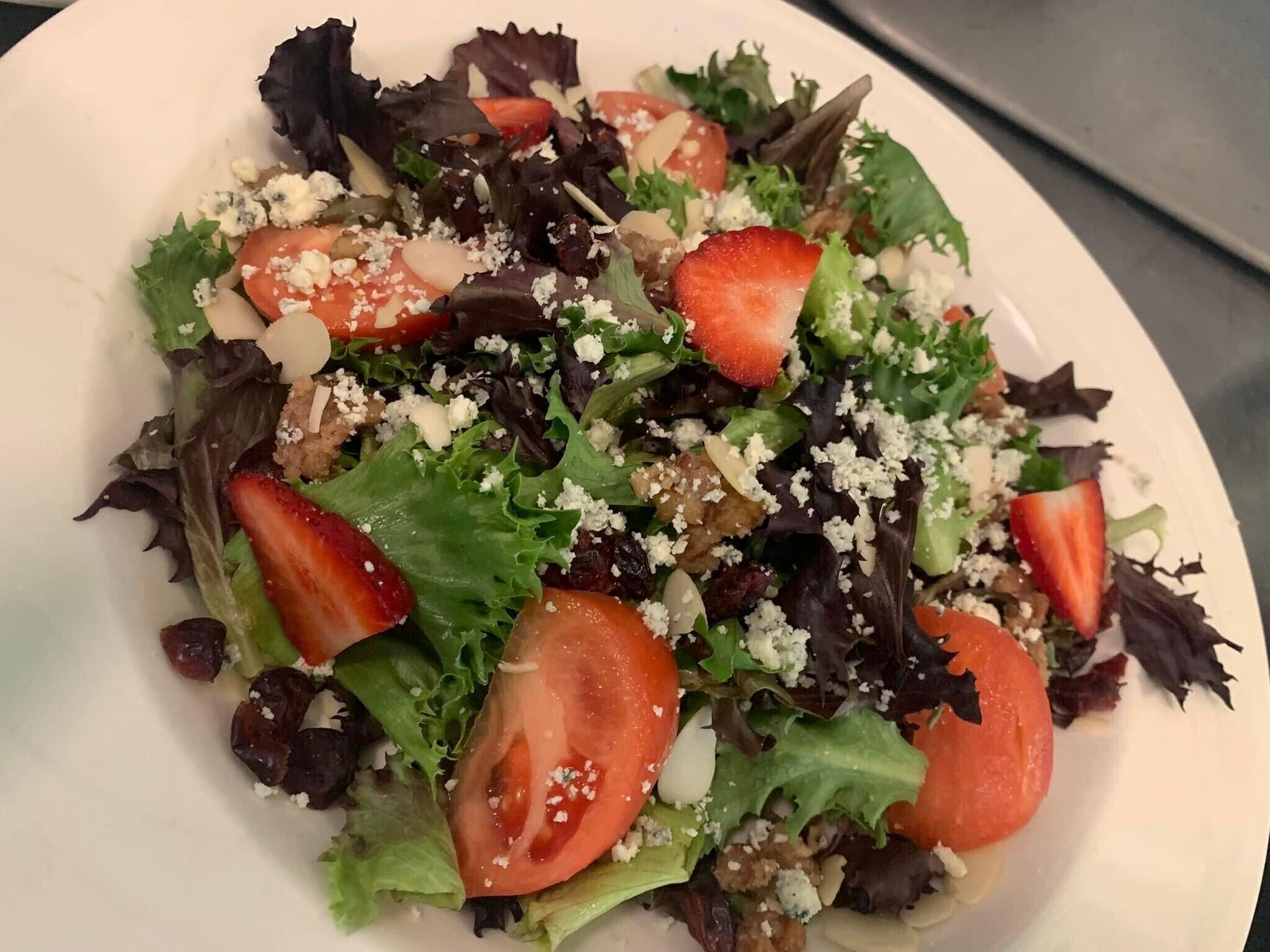 A plate of mixed greens salad with strawberries and crumbled cheese.