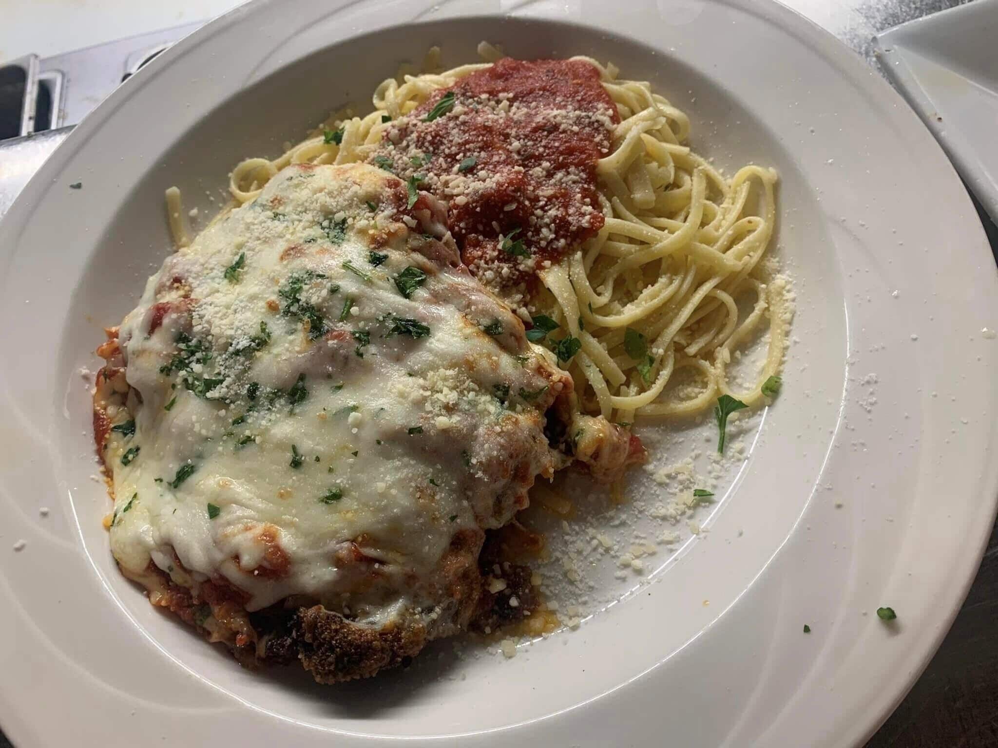 Un plato de espagueti con salsa de carne, posiblemente a la parmesana, adornado con hierbas y queso.