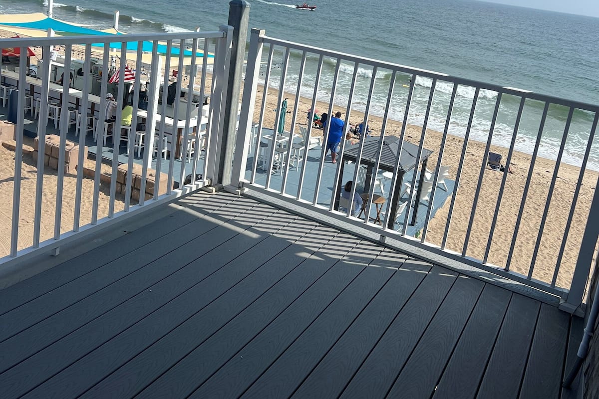 A deck with a view of the beach and ocean, featuring outdoor seating and umbrellas.