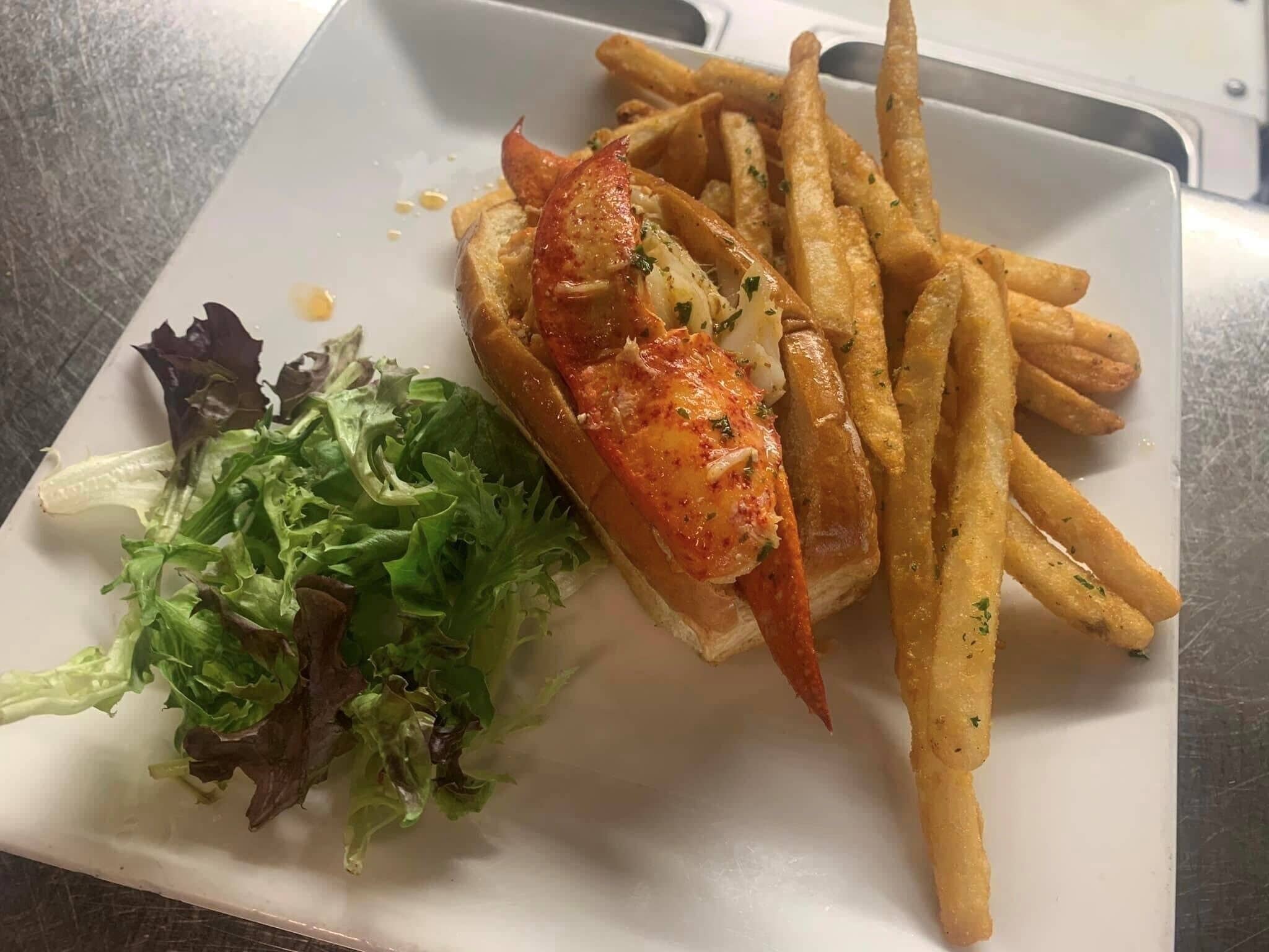 A plate with a lobster tail, fries, and a side salad.
