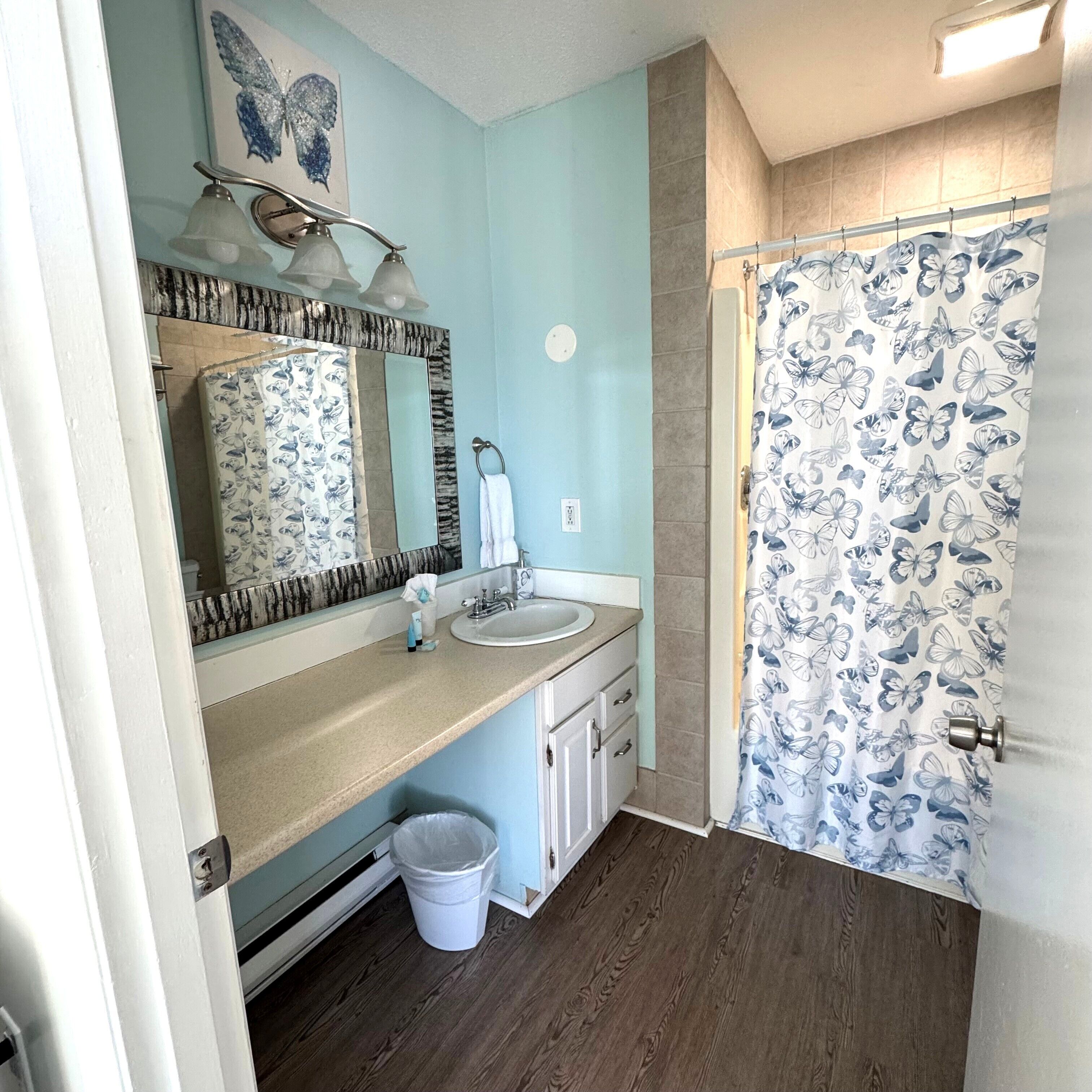 Un baño con lavamanos, espejo y cortina de ducha con estampado de mariposas.
