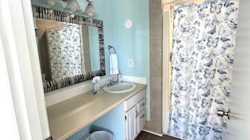 Un baño con lavamanos, espejo y cortina de ducha con estampado de mariposas.