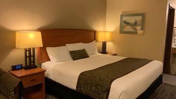 A hotel room with a large bed, two bedside tables with lamps, a nightstand, a clock, and a framed picture on the wall.