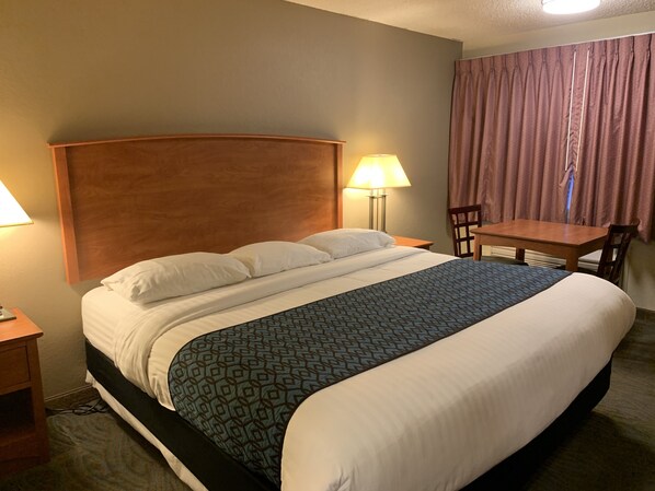 Habitación de hotel con una cama grande, dos lámparas de noche, un cabecero de madera, una mesita pequeña y una silla.