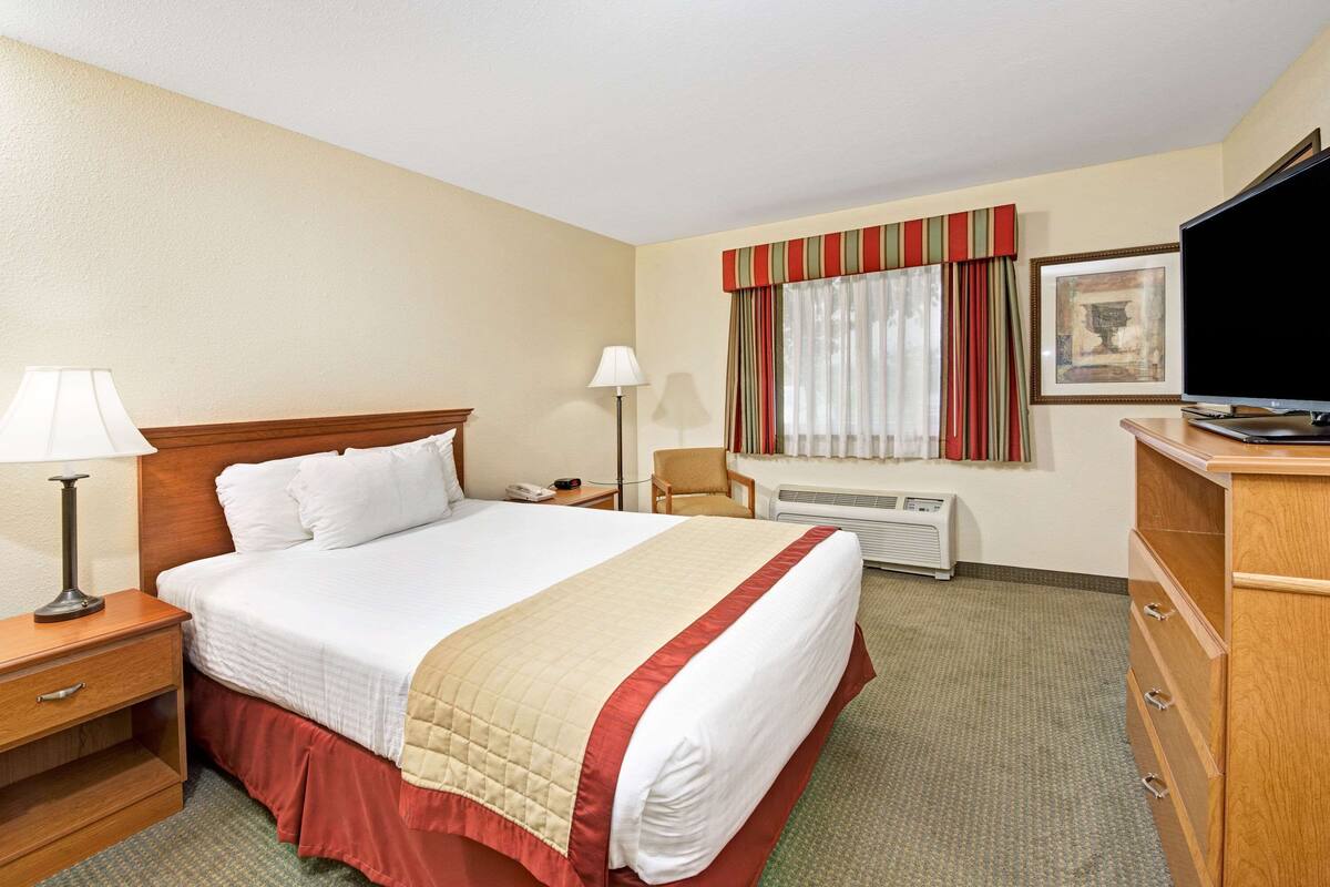 Habitación de hotel con una cama grande, mesitas de noche con lámparas, un televisor, un aparador y una ventana con cortinas.