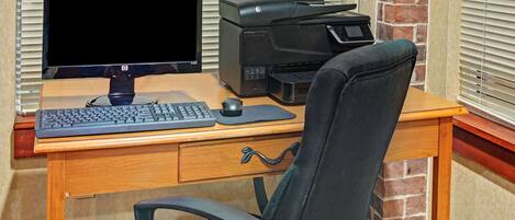 A wooden desk with a desktop computer, a printer, and a black office chair.