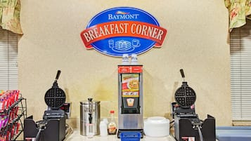 Una estación de desayuno con dos máquinas para hacer gofres, un dispensador de sirope y un dispensador de menús.