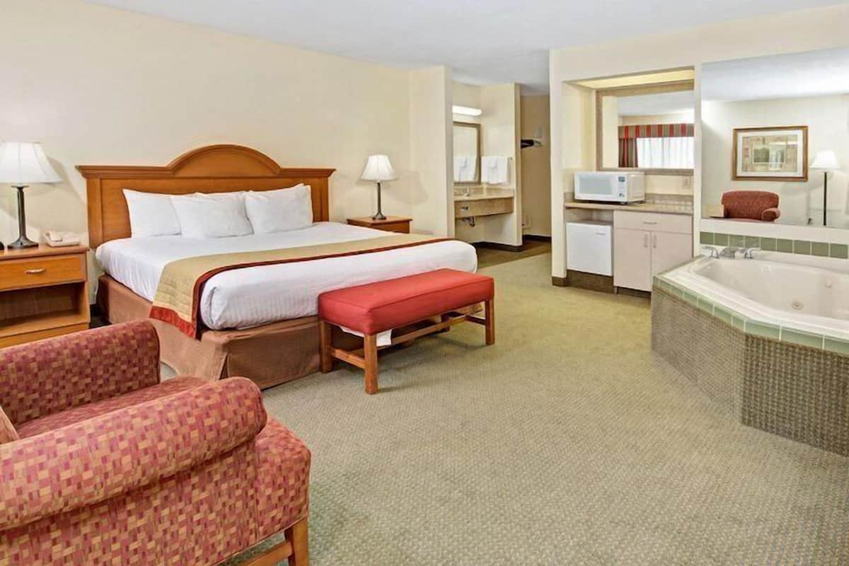 Habitación de hotel con una cama grande, un banco rojo, un sofá, un baño con bañera y un microondas.