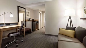 A hotel room with a desk, chair, sofa, lamp, and a small kitchenette. - Country Inn & Suites by Radisson, Washington, D.C. East - Capitol Heights, MD (Capitol Heights)