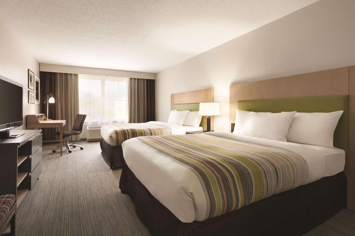 A hotel room with two beds, a desk, a chair, a television, and a window with curtains.