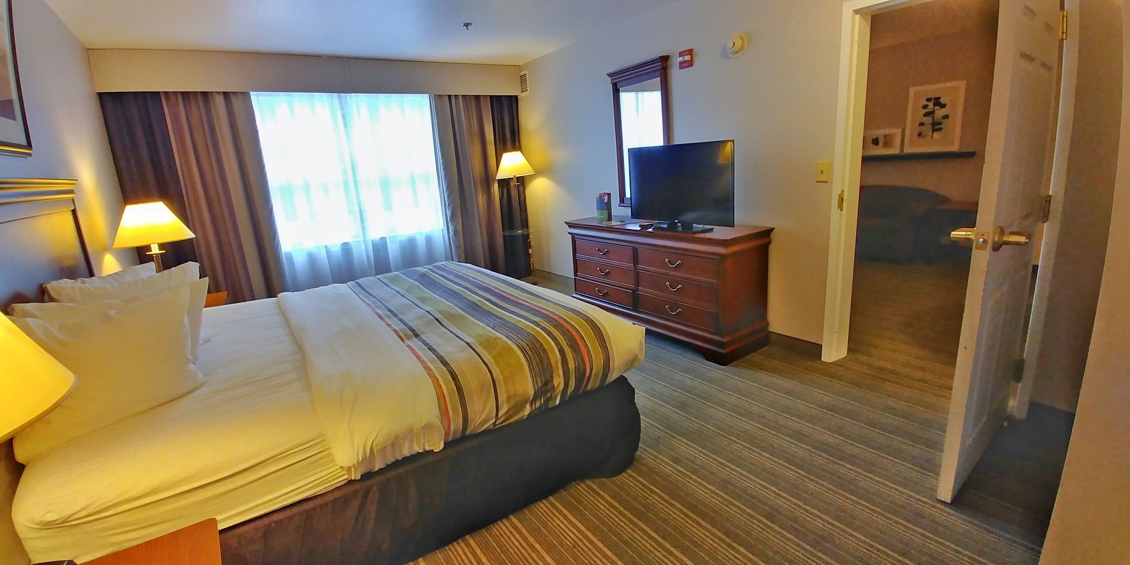 A hotel room with a bed, a dresser, a television, and a door leading to another room.