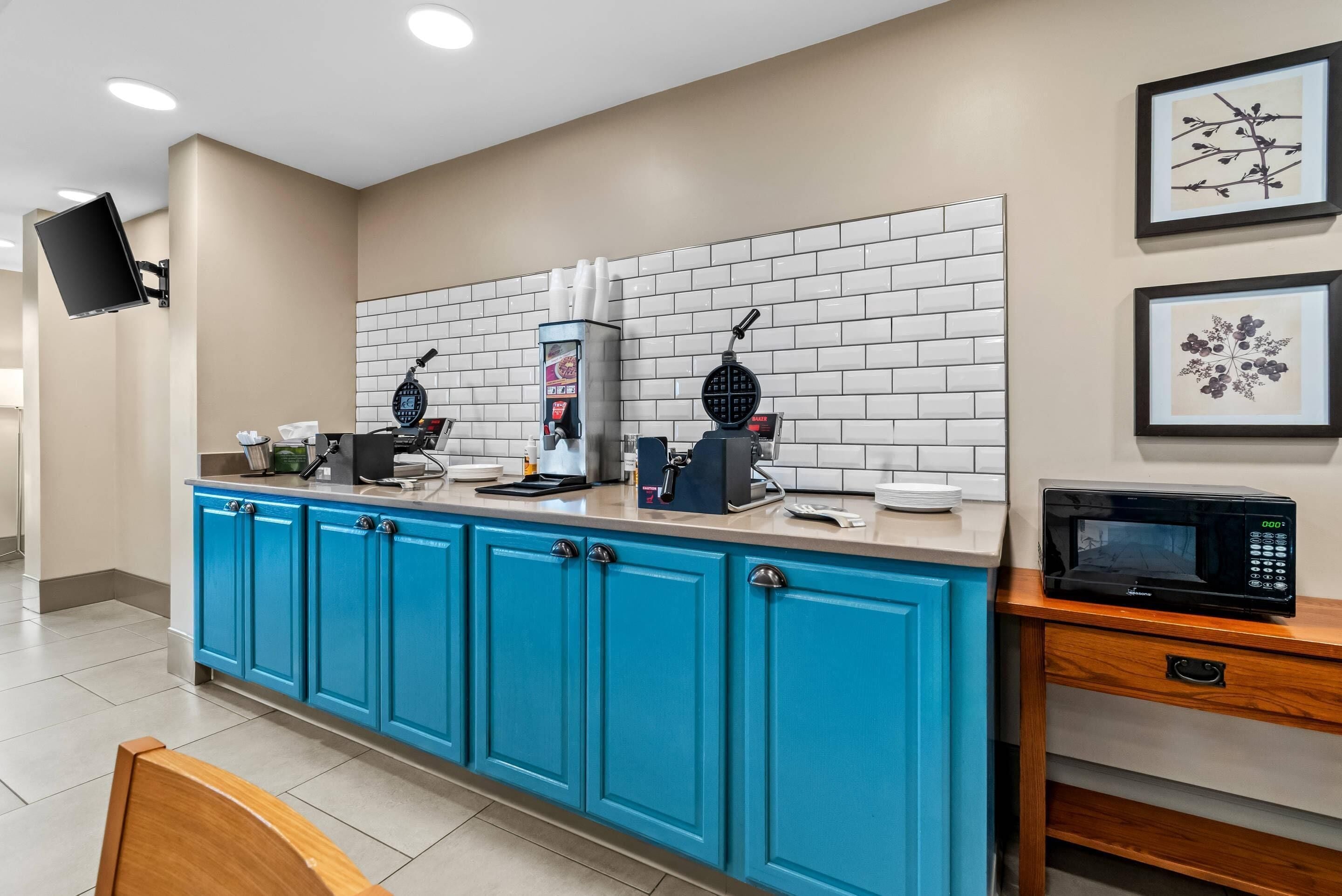 A kitchen area with a coffee machine, waffle maker, and microwave on a blue countertop.