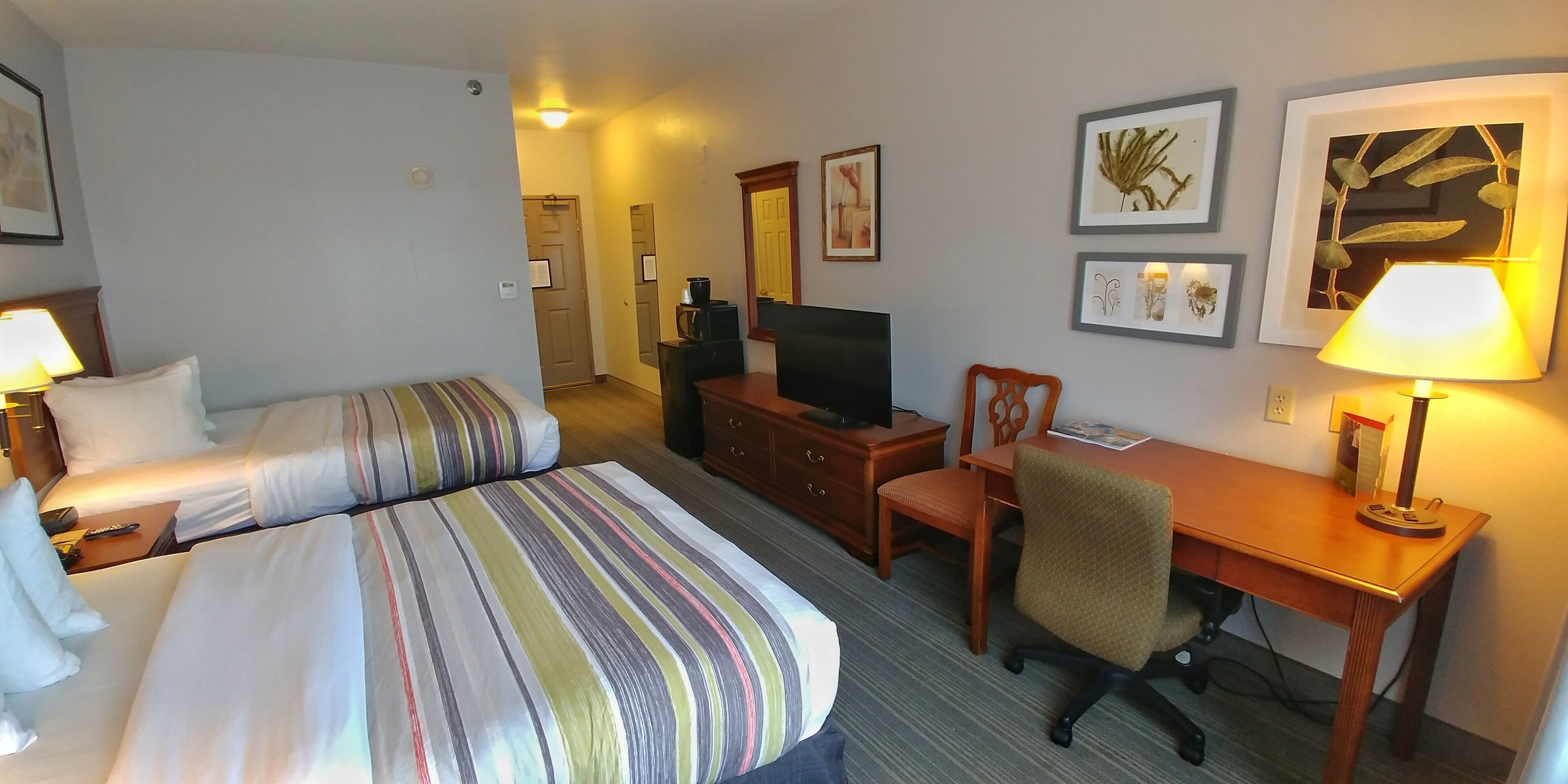 A hotel room with two beds, a desk, a chair, a television, and framed artwork on the walls.