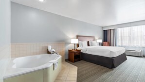 Habitación de hotel con bañera, cama doble, mesita de noche con lámpara y ventana con cortinas.