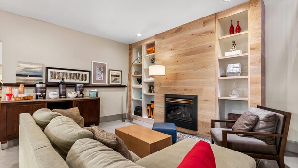 Una sala de estar moderna con un sofá, una mesa de centro y una chimenea. Hay estantes con objetos decorativos y una lámpara.