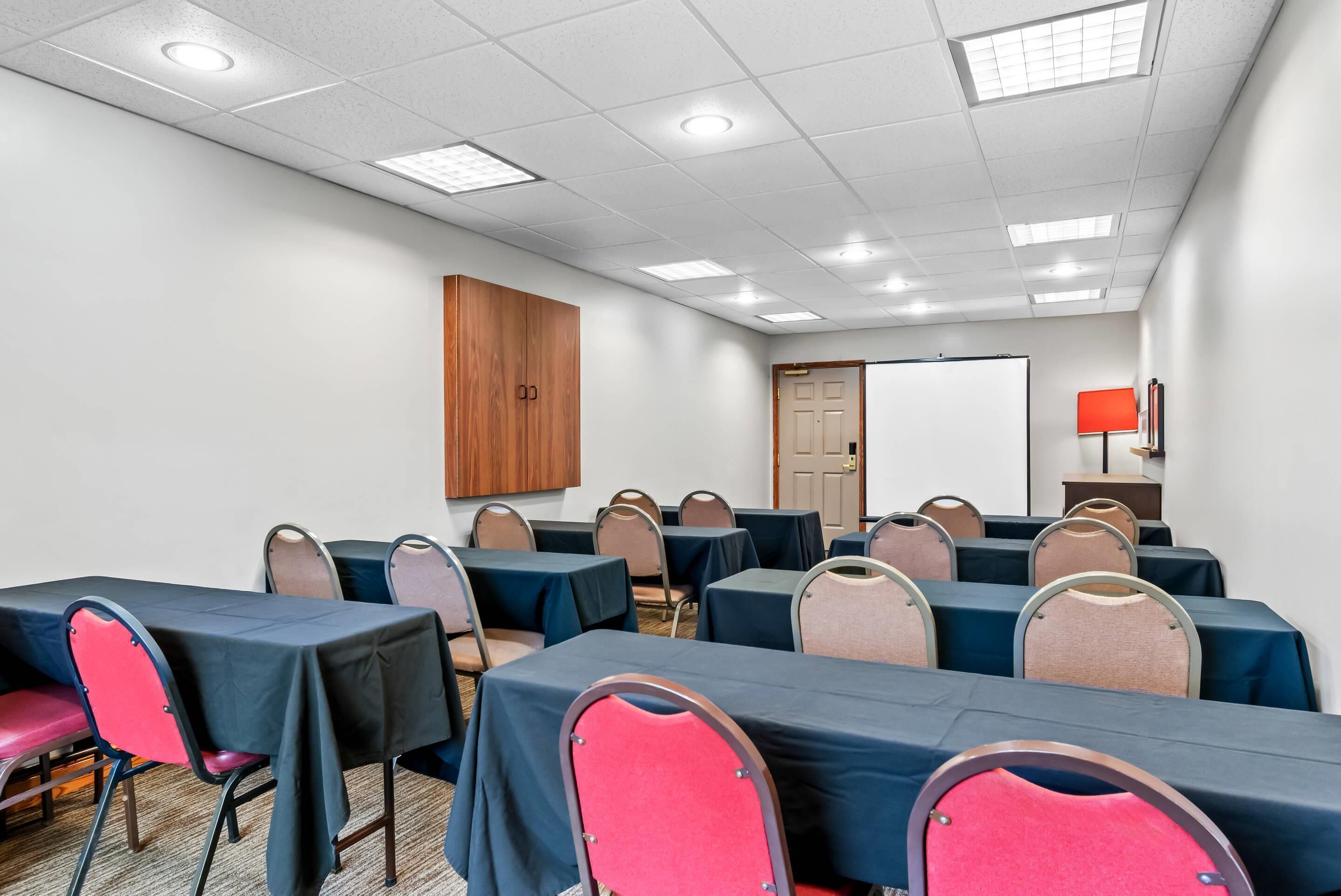 Une salle de conférence équipée de tables et de chaises, d’un buffet en bois, d’un tableau blanc et d’une lampe rouge.