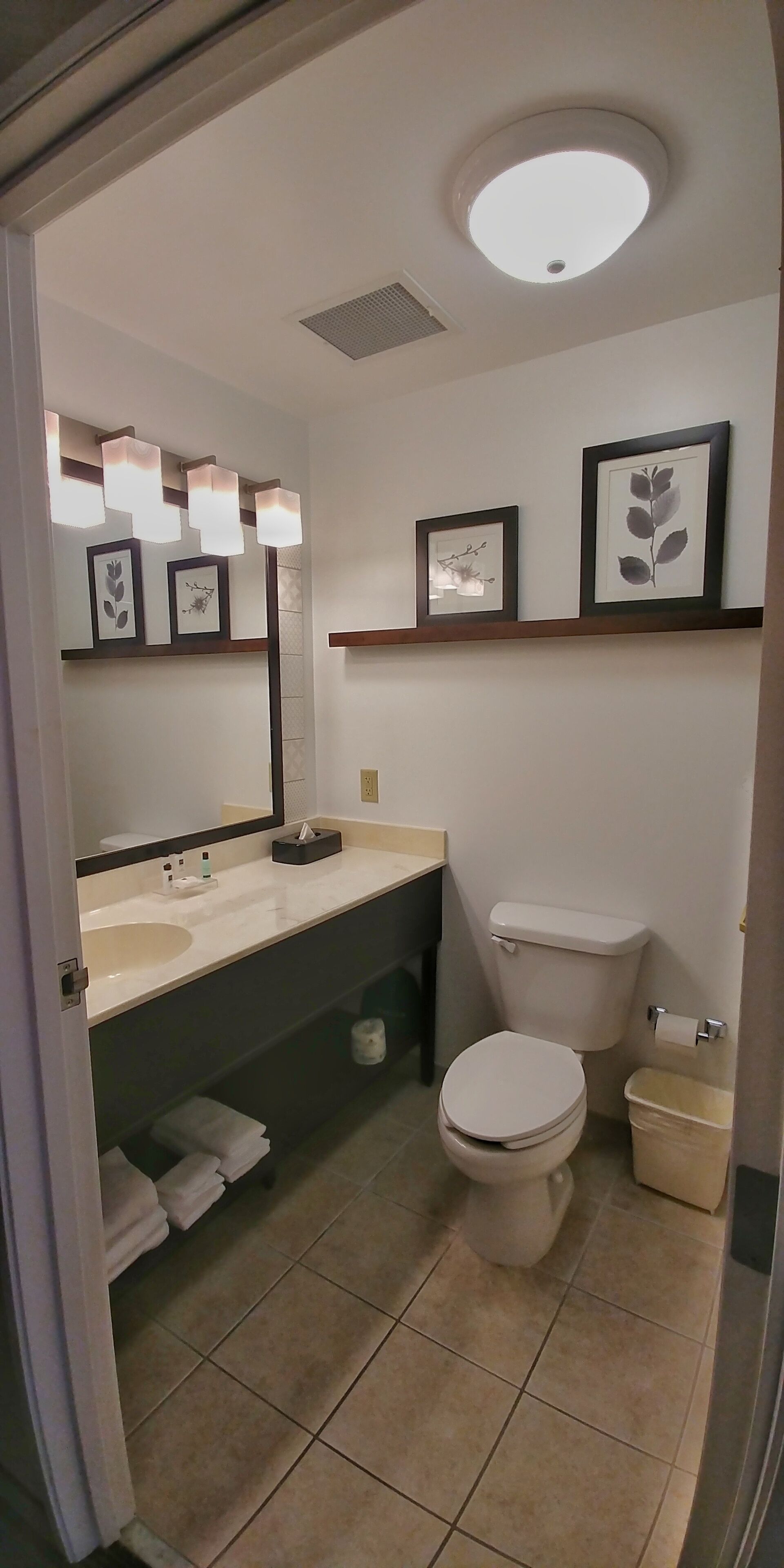 Un baño con lavamanos blanco, espejo, inodoro y un cubo de basura.