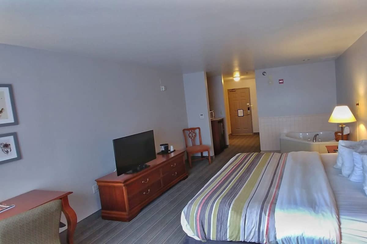 A hotel room with a bed, a TV, a desk, a chair, a bathroom, and a hallway.