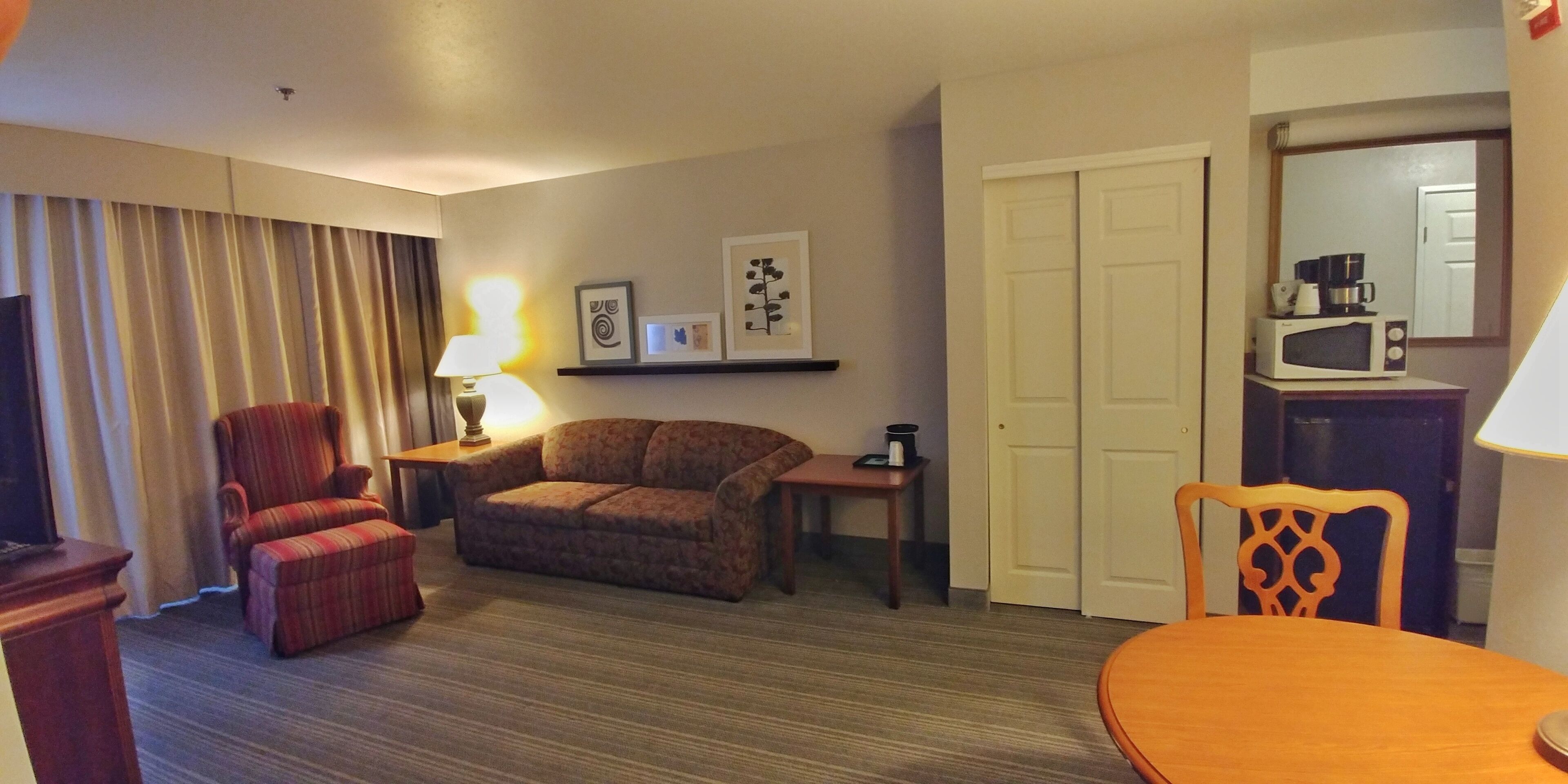 Habitación de hotel con sofá, sillón, mesa de comedor y microondas en la encimera.