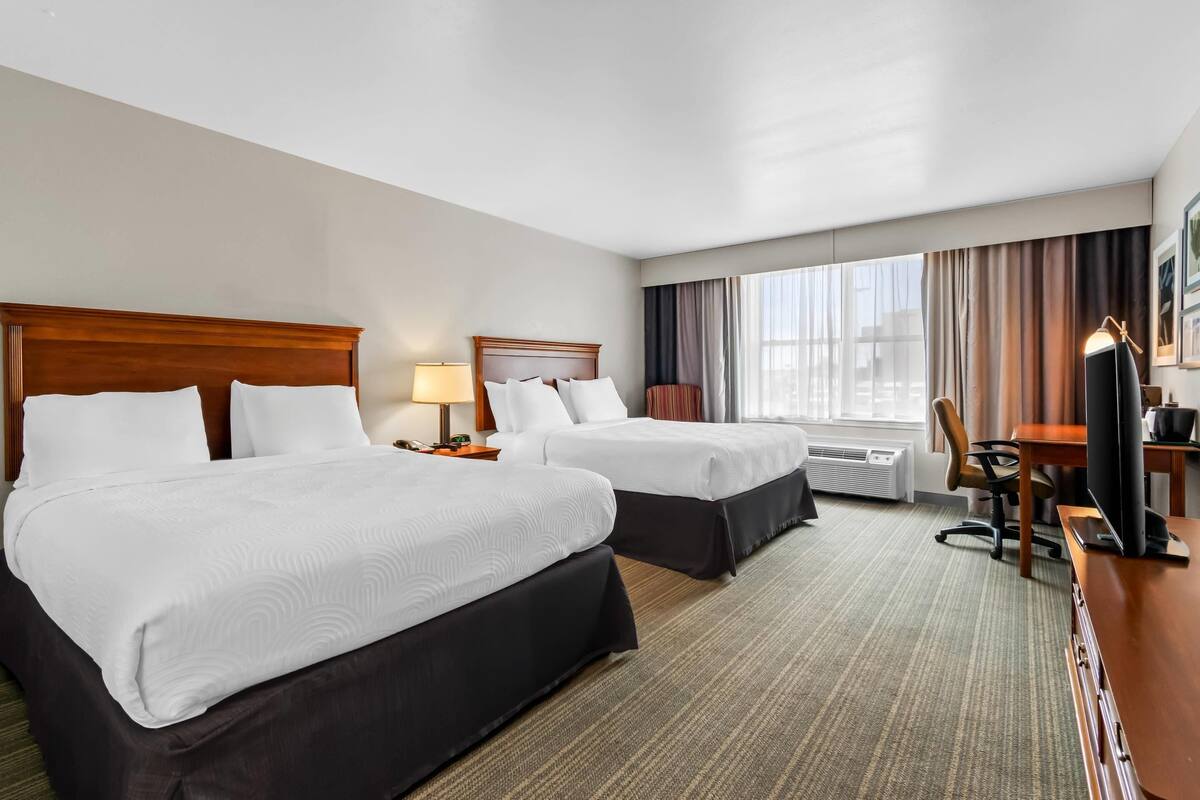 A hotel room with two beds, a desk, a chair, a television, and a window with curtains.