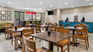 Un restaurante con mesas y sillas de madera, una lámpara colgante roja, un televisor en la pared y una zona de cocina con armarios azules.