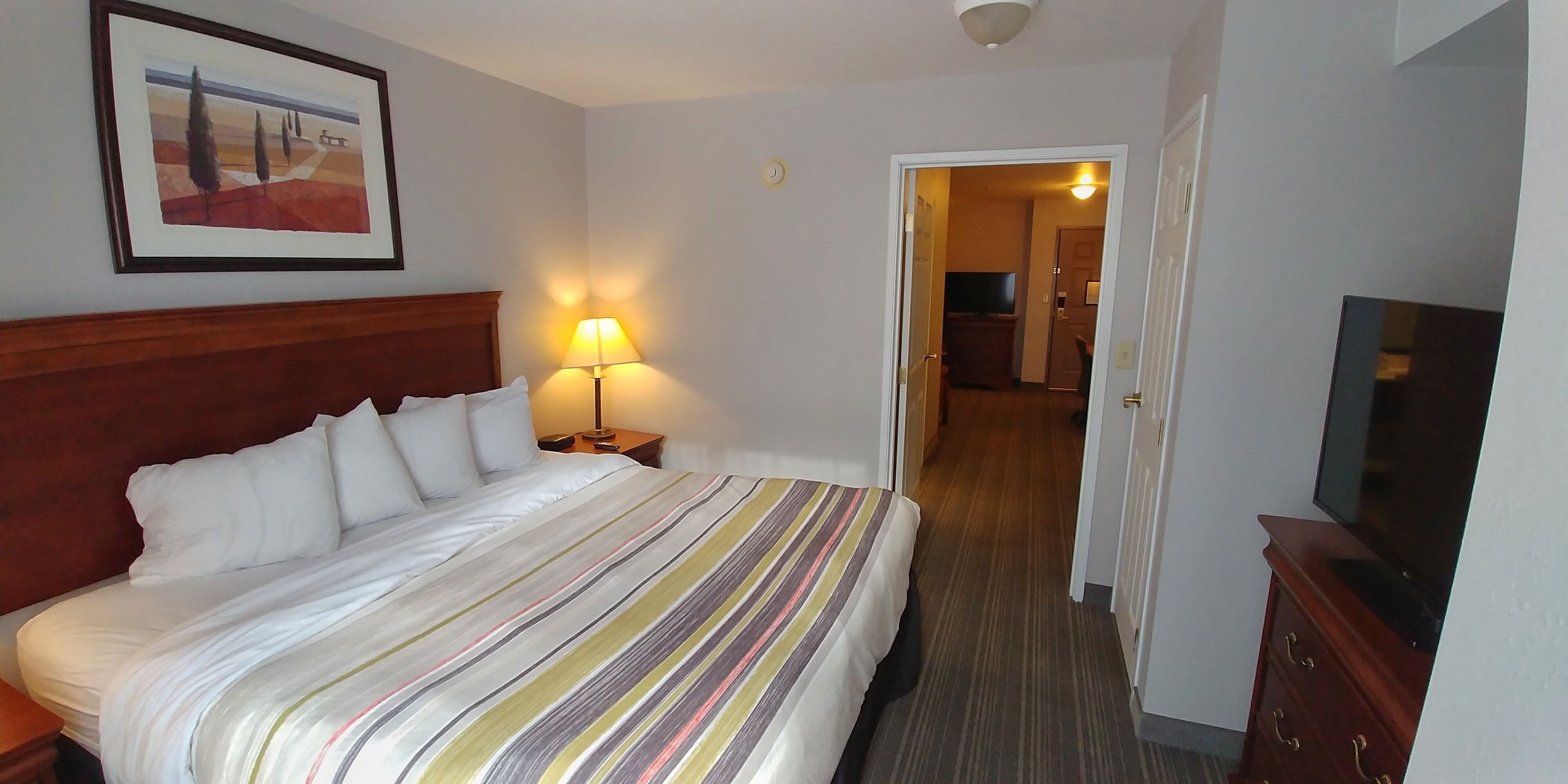 A hotel room with a bed, a bedside lamp, a TV, and a door leading to another room.