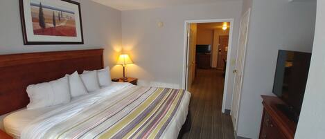 Una habitación de hotel con una cama, una lámpara de noche, un televisor y una puerta que da a otra habitación.