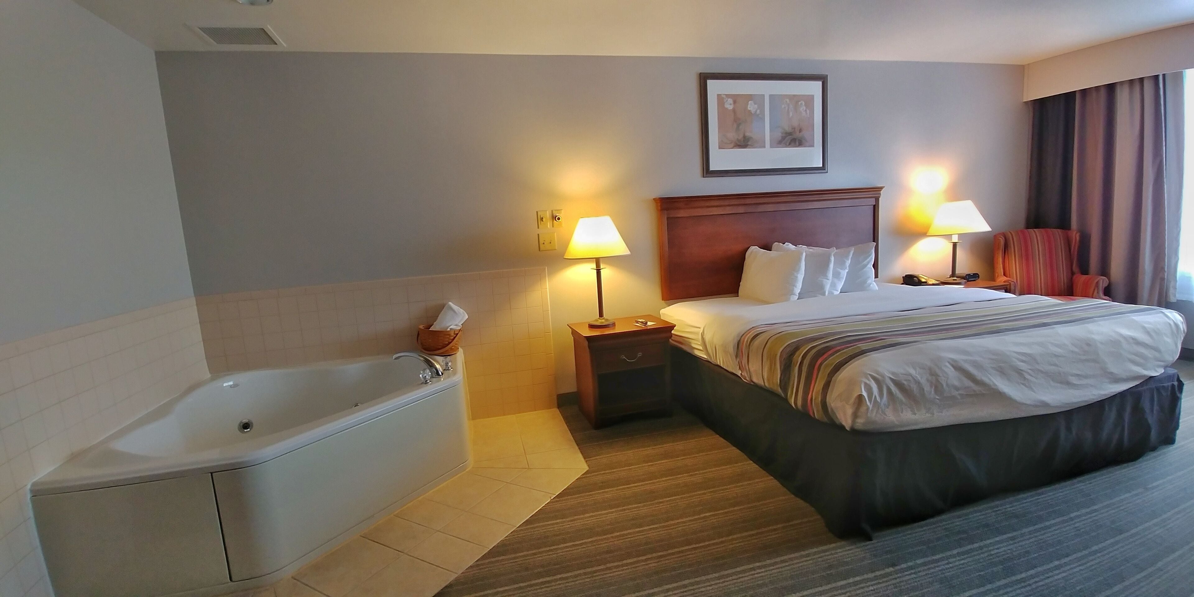 A hotel room with a large bed, a separate bathtub, two bedside lamps, a nightstand, and a framed picture on the wall.