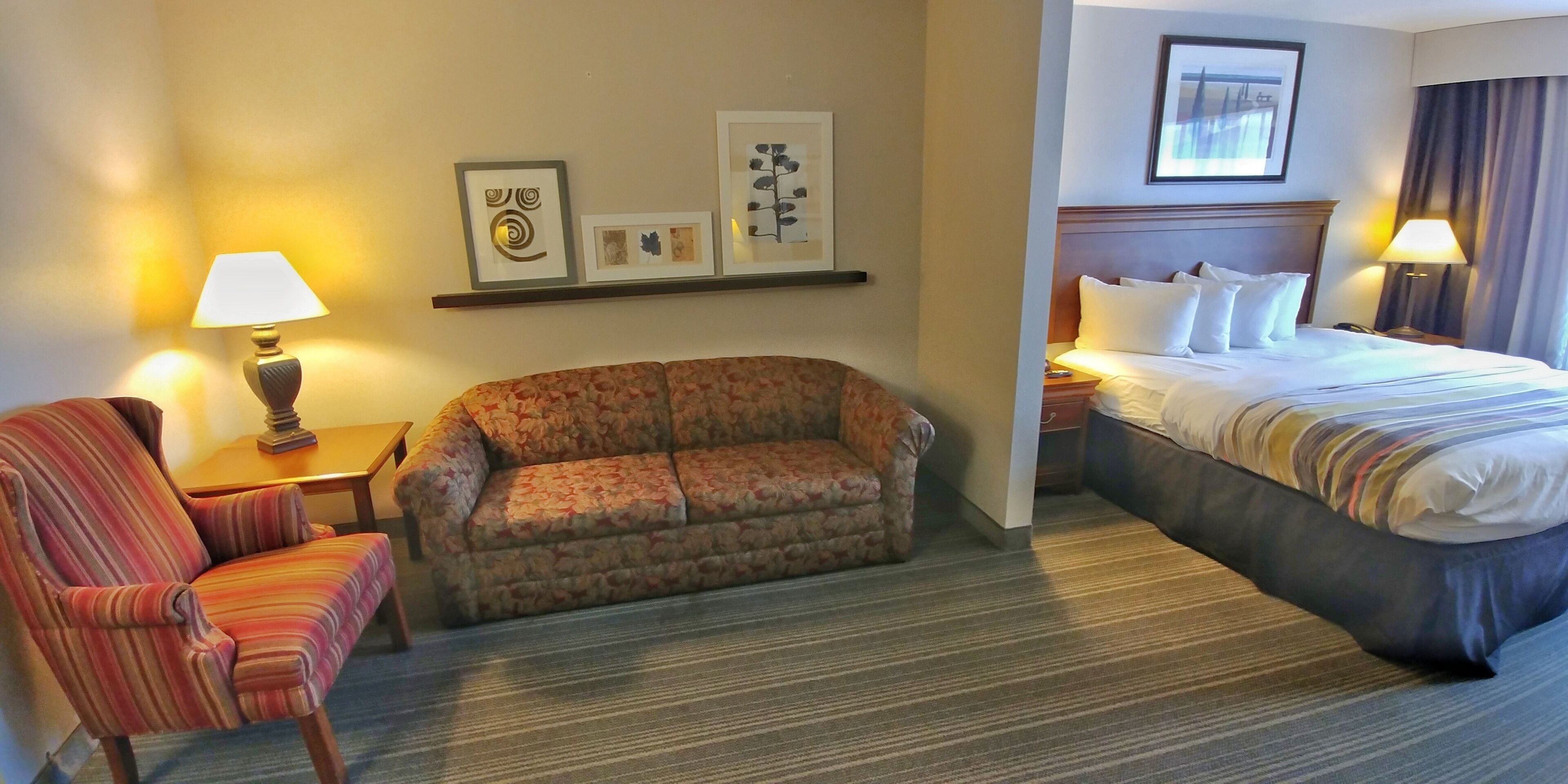A hotel room with a sofa, a chair, a bed, a nightstand, and a lamp.