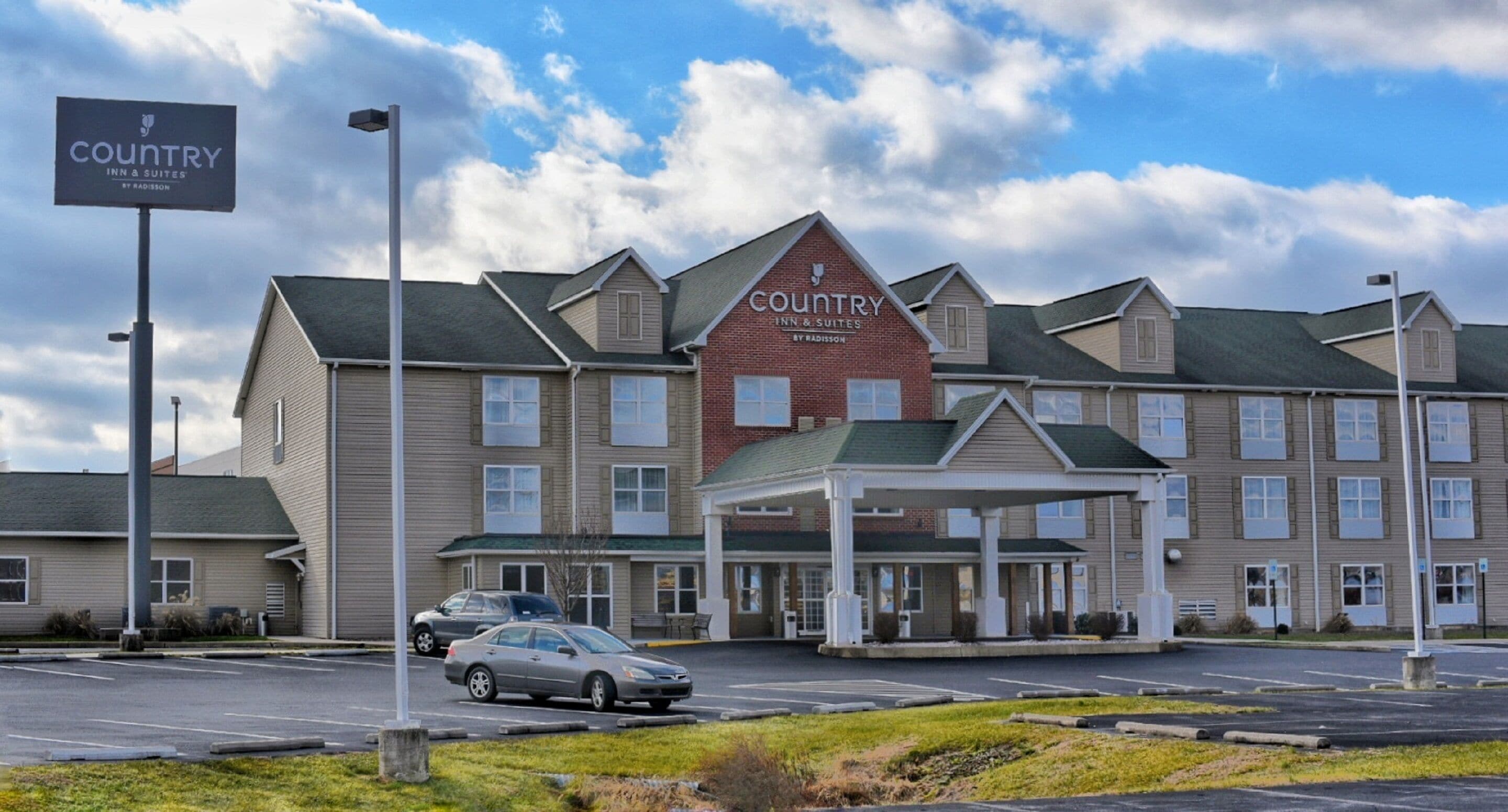 Um hotel Country Inn & Suites com entrada coberta, vários andares e estacionamento.