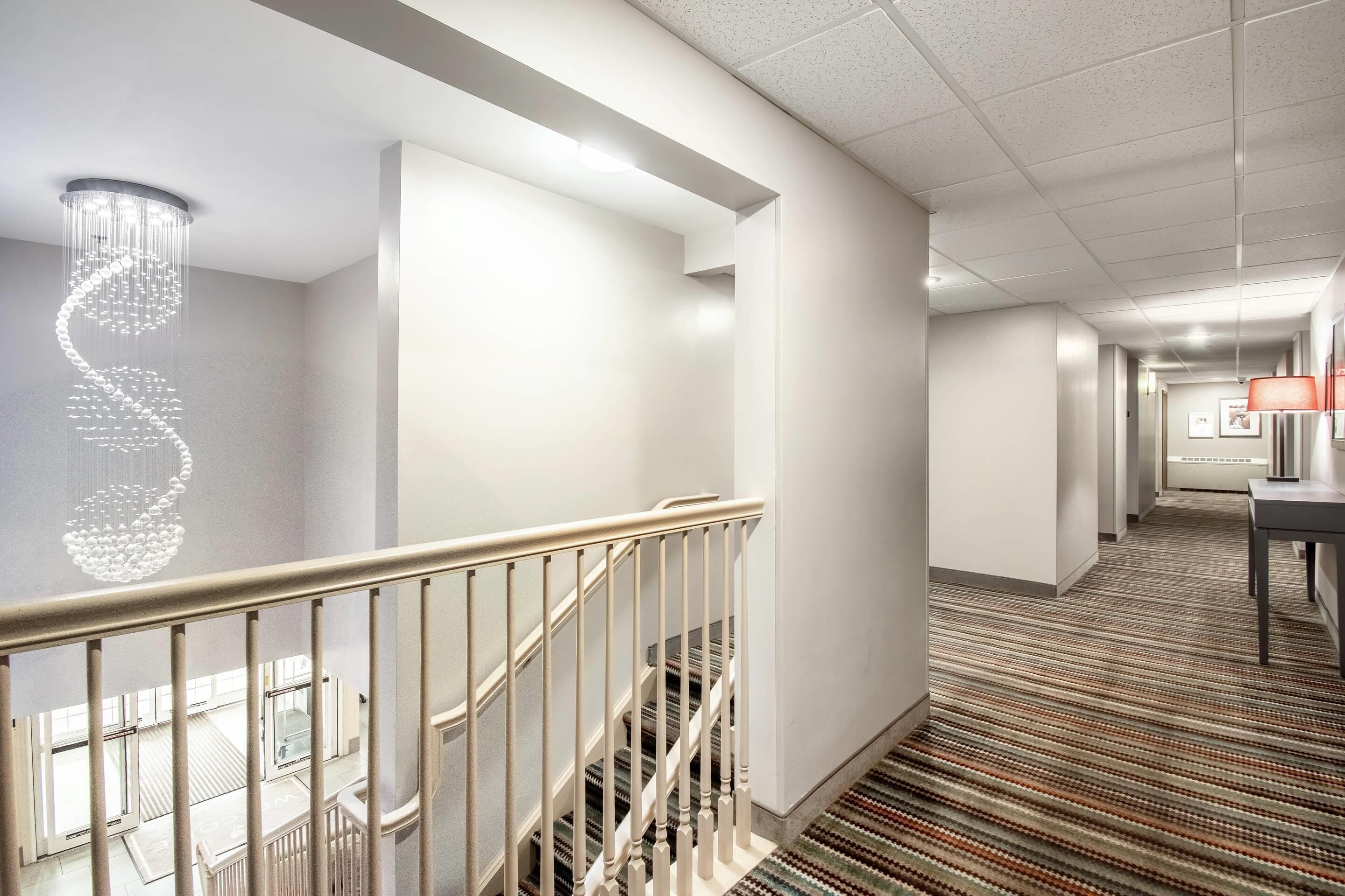 Un pasillo de hotel con una escalera, una araña y una alfombra estampada.