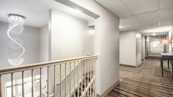 Un pasillo de hotel con una escalera, una araña y una alfombra estampada.