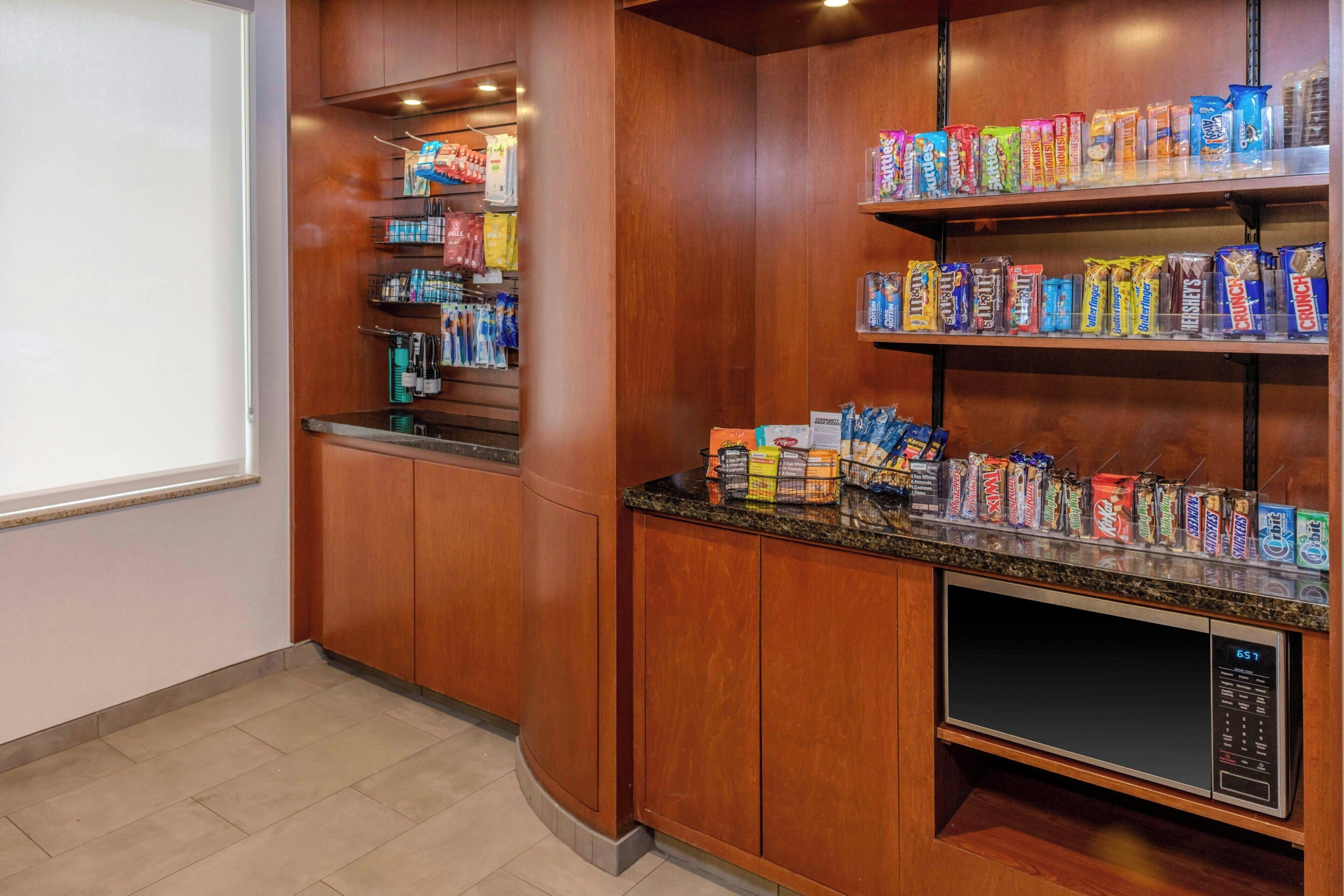 A kitchenette with wooden cabinets, a microwave, and shelves stocked with snacks.
