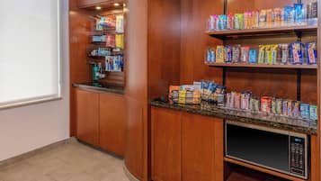 A kitchenette with wooden cabinets, a microwave, and shelves stocked with snacks.