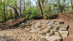 A natural stone water feature with a cascading waterfall, surrounded by a forested area and a metal fence. - Courtyard by Marriott Pittsburgh Greensburg (Greensburg)