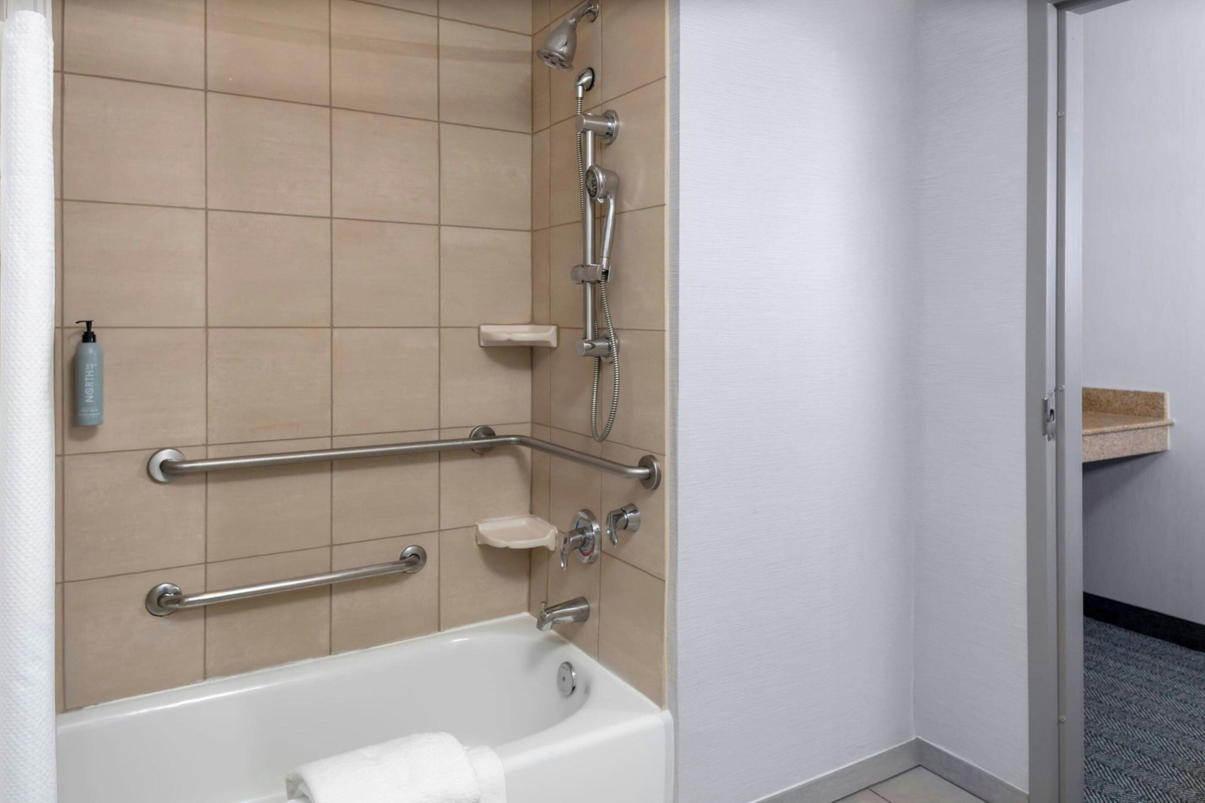 A bathroom with a bathtub, grab bars, a showerhead, and a soap dish.