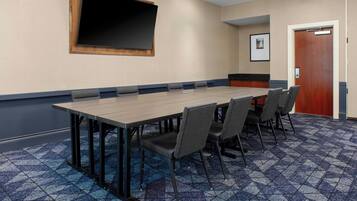 A conference room with a long table, chairs, a flat-screen TV, and a door.