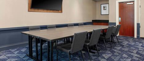 A conference room with a long table, chairs, a flat-screen TV, and a door.