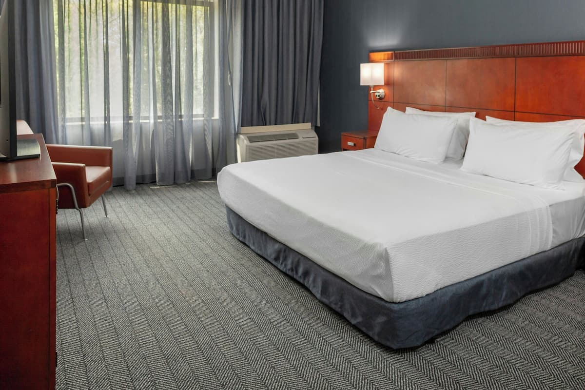 Ein Hotelzimmer mit einem großen Bett, einem Schreibtisch, einem Sessel, einem Nachttisch und einem Fenster mit Vorhängen.