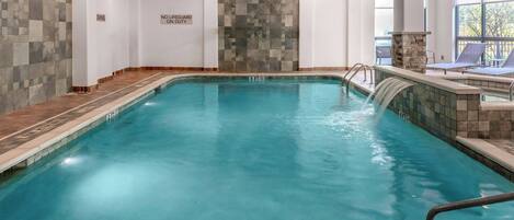 An indoor swimming pool with clear water, tiled walls, and a stone accent wall.