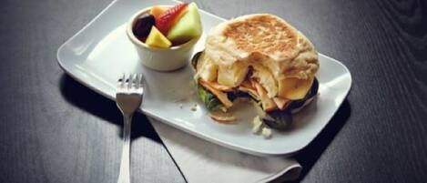 A sandwich on a white plate with a side of fruit.