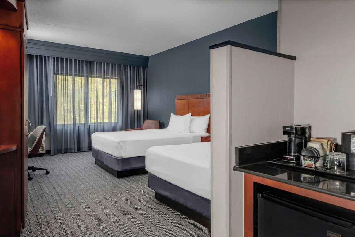 Ein Hotelzimmer mit zwei Betten, einem Schreibtisch mit Kaffeemaschine und Blick ins Freie durch große Fenster.
