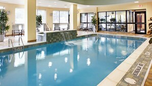 An indoor pool with a waterfall feature, lounge chairs, and a view of the city through large windows. - Courtyard by Marriott Pittsburgh Greensburg (Greensburg)
